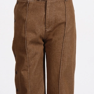 Detail of brown wide-leg trousers with white contrast stitching and side buttons