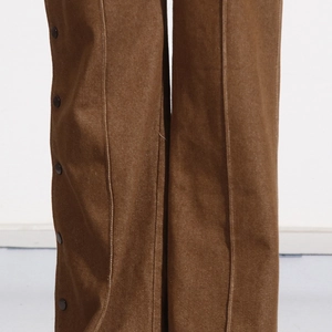 Detail view of brown trousers featuring vertical seams and side snap buttons finish