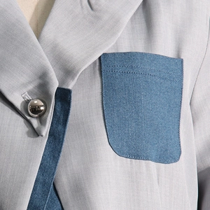 Detail of grey blazer featuring denim contrast pockets and a silver spherical button