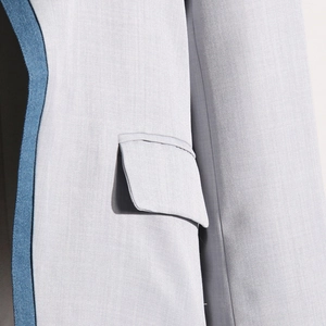 Detail of light gray blazer showing fine woven texture and navy blue contrast piping