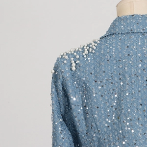 Close-up of light blue fabric with silver sequins and white faux pearl shoulder details