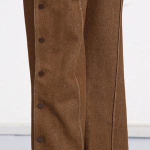Detail of brown wide-leg trousers featuring side snap buttons and white contrast stitching