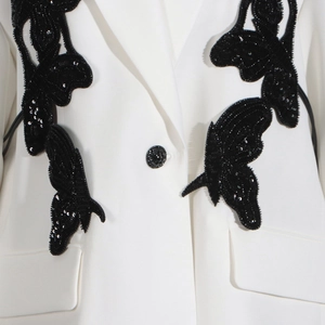 Detail of white blazer featuring black sequined butterfly embroidery and relief button