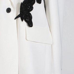 Detail of elegant white blazer featuring a large black sequined butterfly embroidery patch