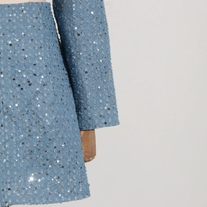 Detail of light blue sequin dress fabric showing glittery texture and long sleeve design
