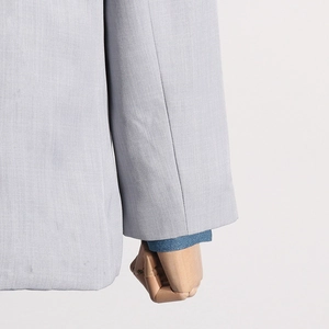 Detail of light gray blazer sleeve with denim shirt cuff layering and fine fabric texture
