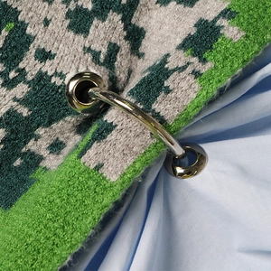 Detail van gebreid shirt met zilveren metalen beslag en groene gebreide textuurafwerking