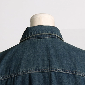 Detailed close-up of stitching on the collar and shoulders of a dark blue denim jacket