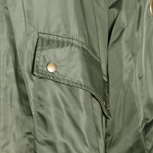 Detailed close-up of olive green parka fabric with a metallic gold snap button pocket