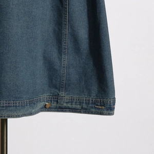 Detail of blue denim jacket hem with reinforced double stitching and retro metal button