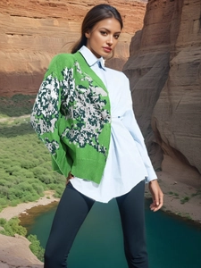 Groene damesvest met jacquardpatroon en blauwe blouse tegen een prachtig berglandschap