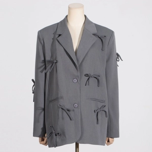 Détail d'un blazer gris oversize avec nœuds papillon en relief sur le col et les manches