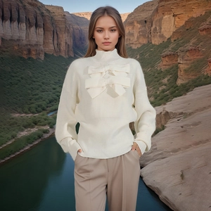Detailed view of white ribbed knit sweater featuring a large decorative bow on the chest
