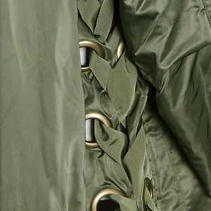 Detail of olive green parka with lace-up ribbon design and metal eyelets on satin fabric