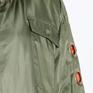 Detail of olive green parka with large pocket, metal eyelets, and orange lining