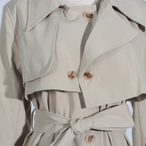 Detail of beige trench coat featuring classic lapels, double storm flaps and marbled buttons