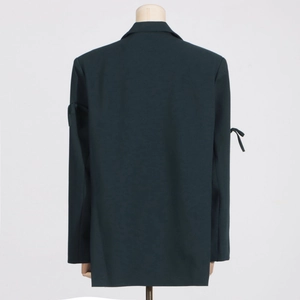 Détail d'un blazer vert foncé avec des poignets à nœuds élégants et une texture raffinée