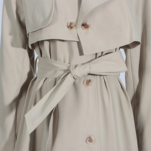 Close-up of khaki trench coat waist with matching tie belt and amber textured button