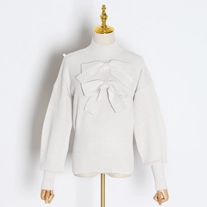Detail of white knit sweater featuring large decorative bows and ribbed high collar