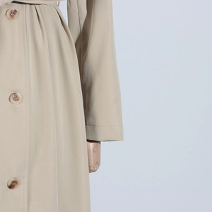 Detail of beige trench coat featuring amber buttons and premium twill fabric texture
