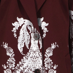 Gros plan du blazer bordeaux avec des motifs baroques argentés et des boutons