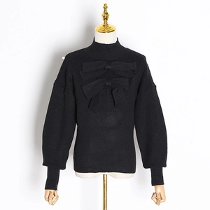 Close-up of black knit top featuring elegant bow accents and ribbed cuffs detailing