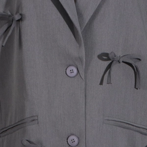 Détail du blazer gris avec revers plat, boutons assortis et ruban de nœud papillon chic
