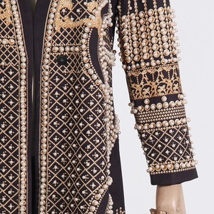 Détail du trench-coat noir de luxe avec broderies dorées et ornements en perles de résine
