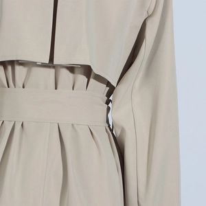 Detail of beige trench coat featuring elegant back storm flap and pleated waist with belt