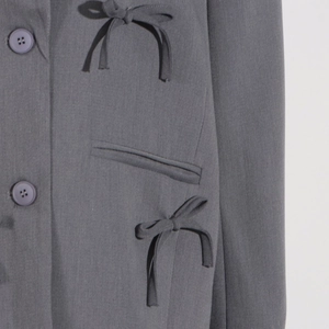 Détail de blazer gris avec nœuds décoratifs, poches passepoilées et boutons assortis
