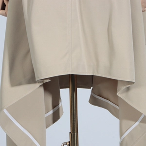 Detailed close-up of the asymmetric hemline and inner white piping of a beige trench coat