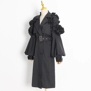 Detail of elegant black trench coat featuring sculptural ruffle shoulders and cinched waist
