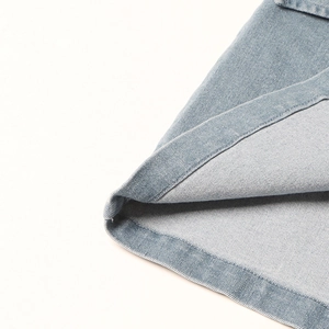 Detailopname van de dubbelgestikte zoom en twill-textuur van de lichtblauwe denim rok