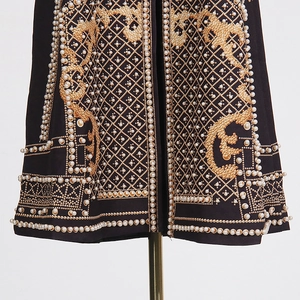 Détails de motifs baroques dorés et de perles sur un manteau noir haute couture