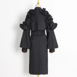 Detail view of sculptural ruffles and layered back panel on a black tailored trench coat