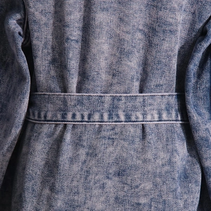 Detailansicht der Taille mit Gürtel und Snow-Wash-Denim-Textur dieser blauen Jacke