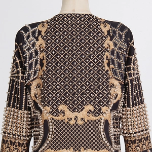 Détail de la broderie dorée et des perles sur un manteau noir à col en V