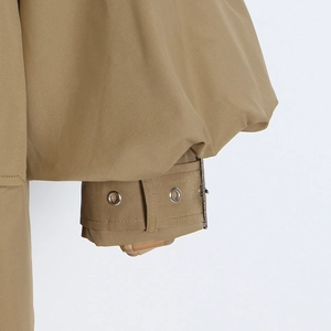 Detailed view of khaki trench coat cuff with adjustable strap and metal eyelet details