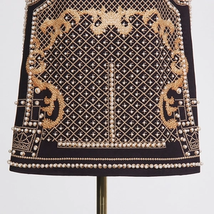 Détail de broderie baroque avec perles blanches et coutures dorées sur manteau noir à col V