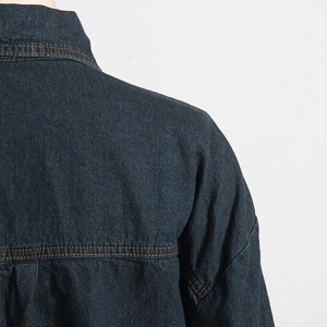 Dettaglio di giacca in denim blu scuro con cuciture a contrasto e spalla scesa