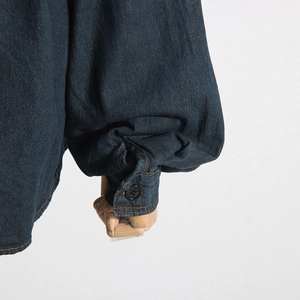 Dettaglio del polsino a sbuffo in denim blu scuro con bottone nero su sfondo bianco