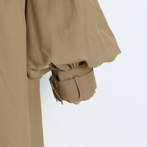 Detail of khaki trench coat sleeve with ruffled puff design and adjustable cuff strap