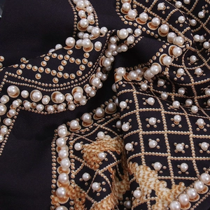 Détail du trench-coat à col en V avec imprimés chaînes dorées et perles blanches
