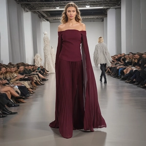 Detail of off-shoulder wine red pleated dress with dramatic long cape sleeves on runway