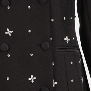 Macro view of black blazer showing rhinestone clover patterns and fabric covered buttons