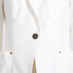 Détail d'un blazer blanc avec un bouton noir et des rivets métalliques argentés aux poches