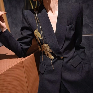 Detailed close-up of intricate gold feather embroidery on a sleek black blazer jacket