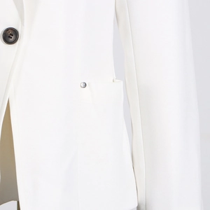Détail du blazer blanc avec des boutons en corne foncée et un clou métallique argenté