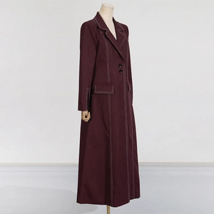 Detail eines burgunderroten Trenchcoats mit weißen Kontrastnähten und Revers-Tasche