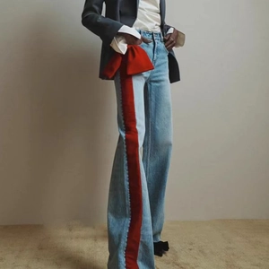 Detail view of light blue denim jeans with red velvet side stripes and a large bow waist accent